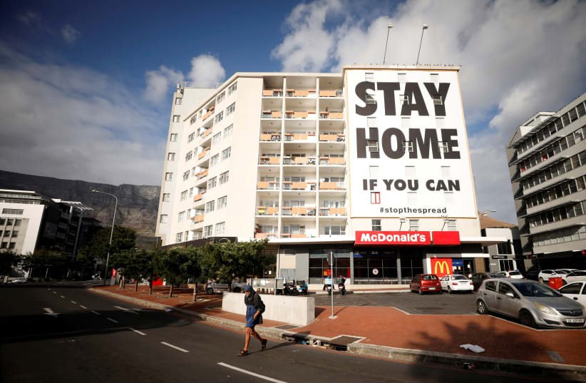 A man walks past a poster covering the side of a building ahead of a 21 day lockdown aimed at limiting the spread of coronavirus disease (COVID-19), in Cape Town, South Africa, March 26, 2020. (photo credit: MIKE HUTCHINGS / REUTERS)