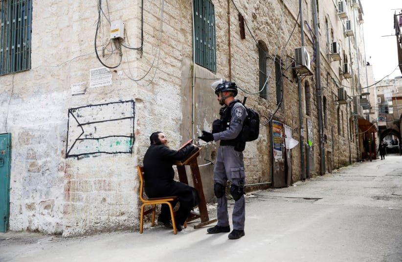 An ultra-Orthodox Jewish man speaks to an Israeli policeman after police removed him from a synagogue before closing it as they enforce restrictions of a partial lockdown against the coronavirus disease (COVID-19) in Mea Shearim neighbourhood of Jerusalem March 30, 2020. (photo credit: RONEN ZVULUN/REUTERS)