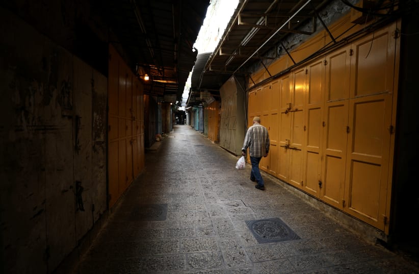 A man walks in an alley inside Jerusalem's Old CIty as shops are closed amid coronavirus restrictions in the walled Old City March 27, 2020 (photo credit: REUTERS/AMMAR AWAD)