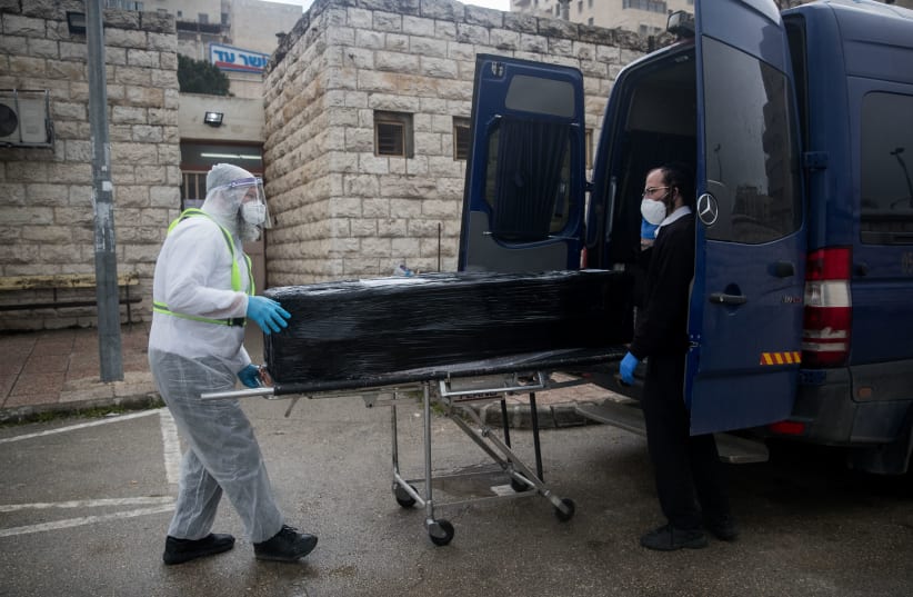 Chevra Kadisha workers wearing protective clothes, carry the body of a patient died from complications of Coronavirus (COVID-19) infection, at the Shamgar Funeral Home in Jerusalem on April 1, 2020 (photo credit: YONATAN SINDEL/FLASH90)