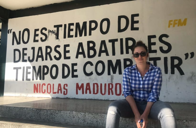 Annika Henroth-Rothstein sits next to a sign with a quote by President Nicolas Maduro in the Venezuelan capital, Caracas. (Annika Henroth-Rothstein) (photo credit: Courtesy)