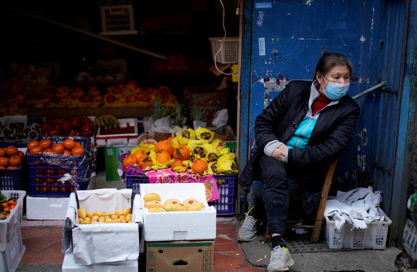 A woman wearing a face mask sits next to a fruit stall at a residential area after the lockdown was lifted in Wuhan, capital of Hubei province and China's epicentre of the novel coronavirus disease (COVID-19) outbreak, April 11, 2020 (photo credit: REUTERS/ALY SONG)
