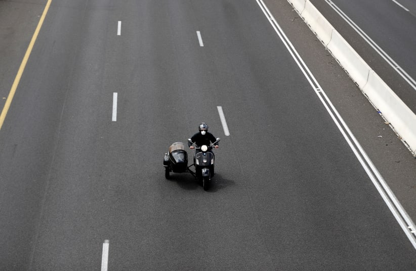 A man wearing a mask drives a motorbike near a roadblock set-up by police as they begin to enforce a national lockdown to fight the spread of the coronavirus disease (COVID-19) on a road leading to Jerusalem, near Ein Hemed, Israel April 7, 2020. (photo credit: REUTERS/Ronen Zvulun)