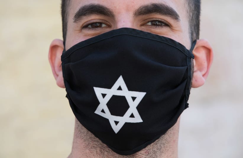 A man wears a face mask  with David Star at the Nachlaot Neighborhood in Jerusalem on April 12, 2020. A full closure on 17 Jerusalem Neighborhoods went into effect today at noon in efforts to contain the spread of the coronavirus. (photo credit: NATI SHOCHAT/FLASH 90)