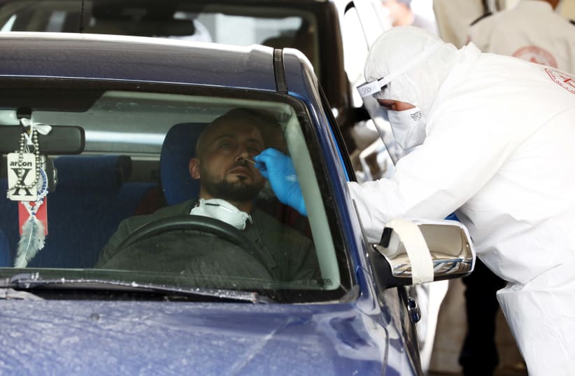 A nose-swab is taken from a driver at a drive-through coronavirus testing station in east Jerusalem, amid coronavirus disease (COVID-19) outbreak April 2, 2020. (photo credit: AMMAR AWAD / REUTERS)