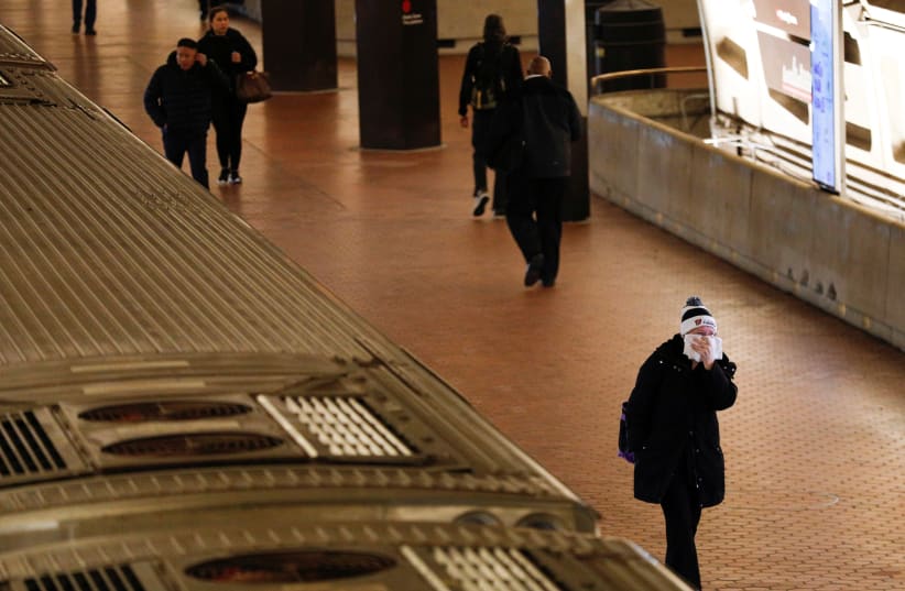 A morning commuter holds a towel covering a face after departing from a Metro train car, as Mayor Muriel Bowser declared a State of Emergency due to the coronavirus disease (COVID-19), inside the Metro Center underground subway station, in Washington, U.S., March 16, 2020 (photo credit: REUTERS/TOM BRENNER)