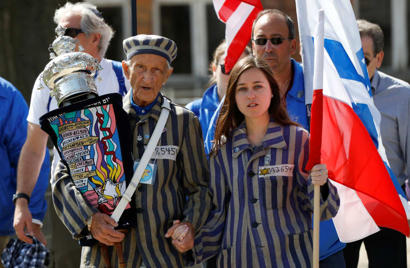 Holding a Torah scroll, Ed Mosberg marches with his granddaughter on the March of the Living in 2018. (photo credit: MARCH OF THE LIVING)