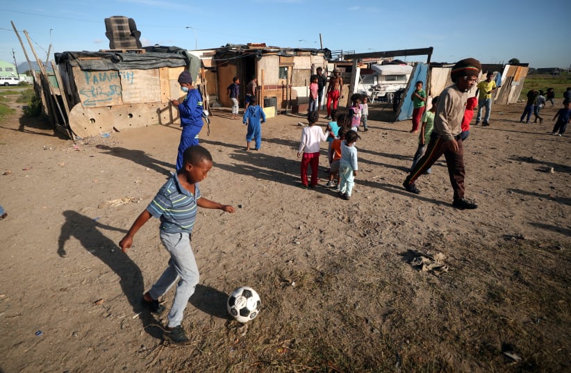 A township child plays soccer as residents wait to receive food packages handed out by a non governmental organisation during a 21-day nationwide lockdown aimed at limiting the spread of coronavirus disease (COVID-19) in Cape Town, South Africa, April 17, 2020. (photo credit: MIKE HUTCHINGS / REUTERS)