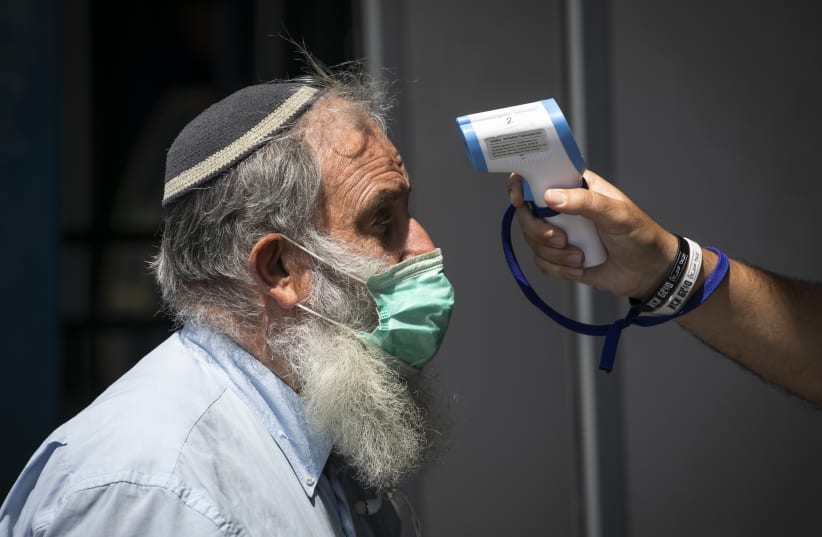 A security guard checks the temperature of passengers at the entrance to the central bus station in Jerusalem, on April 20, 2020. (photo credit: OLIVIER FITOUSSI/FLASH90)