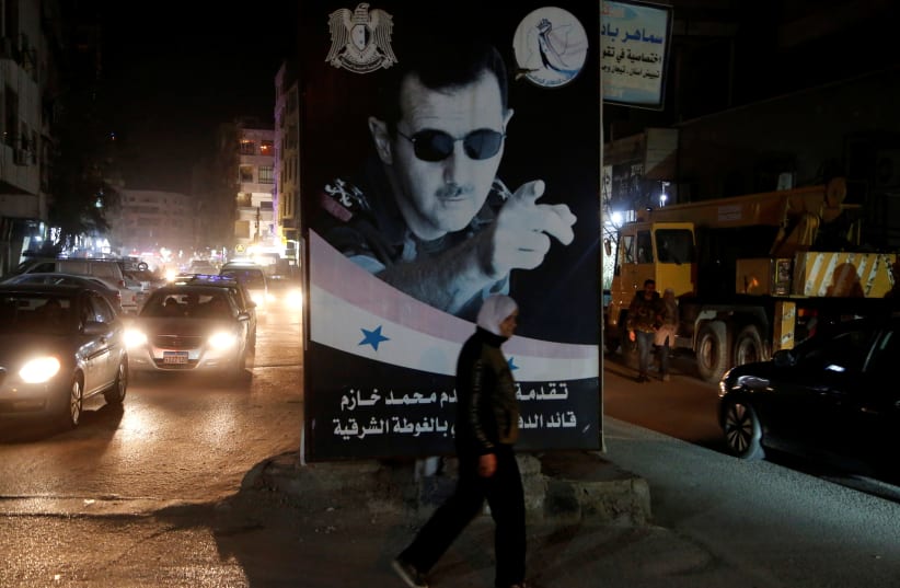 A woman walks past a poster depicting Syria's President Bashar al-Assad in Damascus, Syria March 5, 2020 (photo credit: REUTERS/YAMAM AL SHAAR)