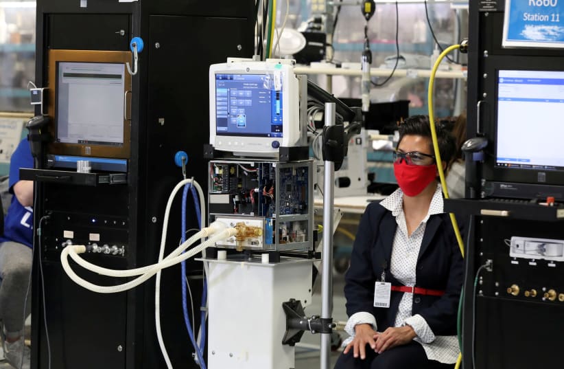An employee wearing a face mask sits next to a GE Carescape R860 ventilator in an assembly and testing area at a GE Healthcare manufacturing facility during the global coronavirus disease (COVID-19) outbreak in Madison, Wisconsin, U.S. April 21, 2020 (photo credit: REUTERS)