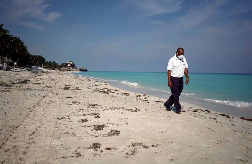 A SECURITY AGENT wearing a protective mask walks on the beach, in Varadero, Cuba, earlier this month.  (photo credit: ALEXANDRE MENEGHINI/REUTERS)