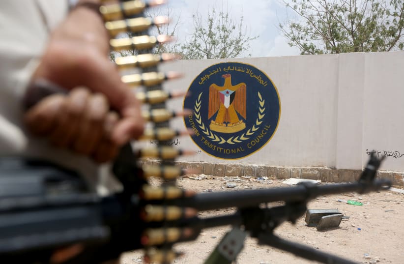 A Yemeni government soldier holds a weapon as he stands by an emblem of the STC at the headquarters of the separatist Southern Transitional Council in Ataq (photo credit: ALI OWIDHA/ REUTERS)