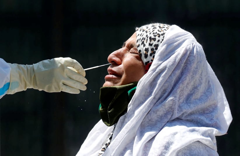 A woman reacts as a doctor wearing a protective glove takes a swab to test for coronavirus disease (COVID-19) at a residential area in Srinagar (photo credit: REUTERS/DANISH ISMAIL)