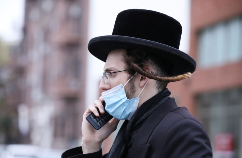 An Orthodox Jewish man wears a mask while talking on a cellphone in the Orthodox Jewish community of the Borough Park neighborhood during the outbreak of the coronavirus disease (COVID19) in the Brooklyn borough of New York, U.S., April 30, 2020. (photo credit: REUTERS/CAITLIN OCHS)
