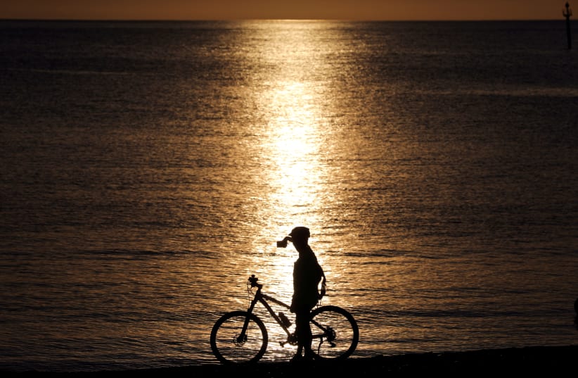 A cyclist takes a picture at the Barceloneta beach during the hours in which individual exercise is allowed outdoors, for the first time since the lockdown was announced, amid the coronavirus disease (COVID-19) outbreak, in Barcelona, Spain, May 2, 2020. (photo credit: REUTERS/NACHO DOCE)