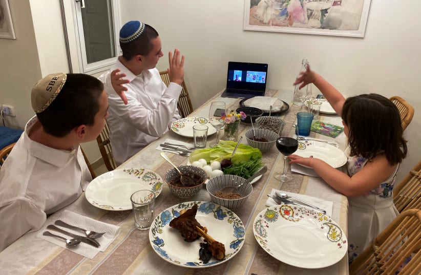 Three siblings in Mevaseret Zion, near Jerusalem, wave to their their grandmother in Haifa as she joins their Passover Seder via Zoom  (photo credit: REUTERS/DAN WILLIAMS)