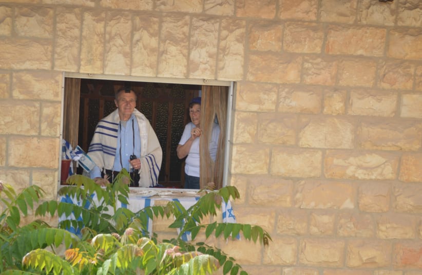 THE WRITER and her husband peek from the window while taking part in a minyan on their street. (photo credit: MALKIEL GLASSER)