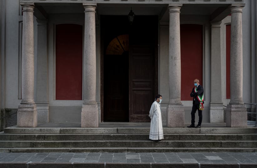 Priest Don Giuseppe Castelvecchio and Mayor of San Fiorano Mario Ghidelli wear masks as they wait outside a church ahead of an evening mass. May 4, 2020 (photo credit: MARZIO TONIOLO/VIA REUTERS)