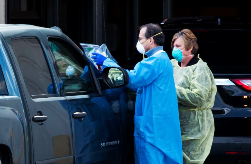 Health workers start the process to test people in a car as they use a newly approved saliva-based coronavirus disease (COVID-19) test at a testing site during the outbreak of the coronavirus disease (COVID-19) in Edison, New Jersey, U.S., April 15, 2020 (photo credit: REUTERS/EDUARDO MUNOZ)
