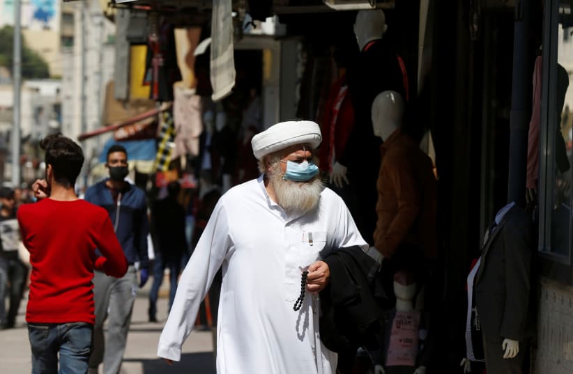 A man wears a protective face mask as he walks along the main market in downtown after the government eased the restrictions on movement aimed at containing the spread of the coronavirus in Amman, Jordan (photo credit: MUHAMMAD HAMED/REUTERS)