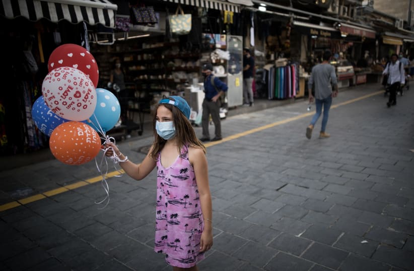 An Israeli girl stands as she hold balloons at the Mahane Yehuda Market in Jerusalem on May 13, 2020. (photo credit: YONATAN SINDEL/FLASH90)