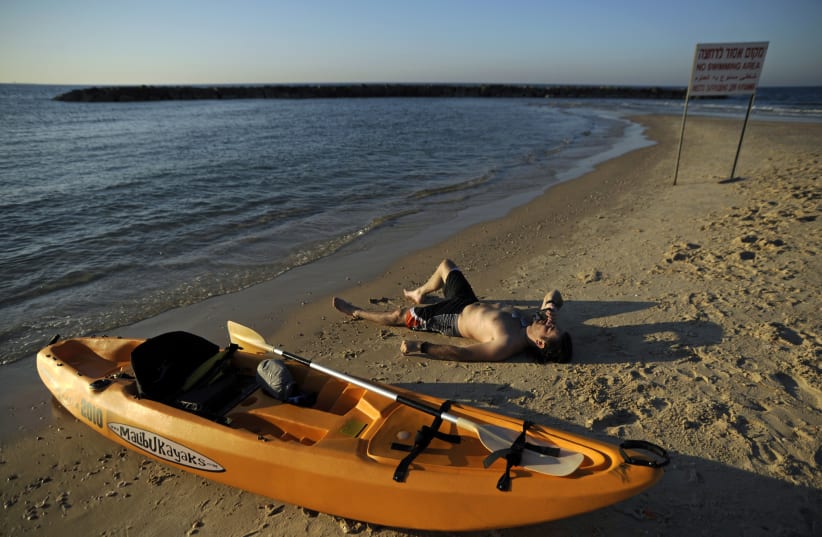 A beach-goer lies near a kayak on the shore of the Mediterranean in the southern Israeli city of Ashkelon (photo credit: REUTERS/AMIR COHEN)