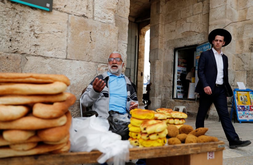 An orthodox Jewish man walks next to a vendor at one of the entrances to Jerusalem's Old City March 9, 2020 (photo credit: RONEN ZVULUN/REUTERS)