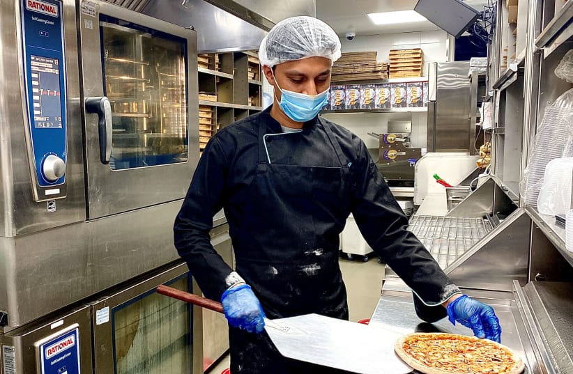 A worker wearing a protective face mask and gloves prepares food for delivery following the coronavirus outbreak. Dubai, UAE, May 12, 2020.  (photo credit: REUTERS/ABDEL HADI RAMAHI)