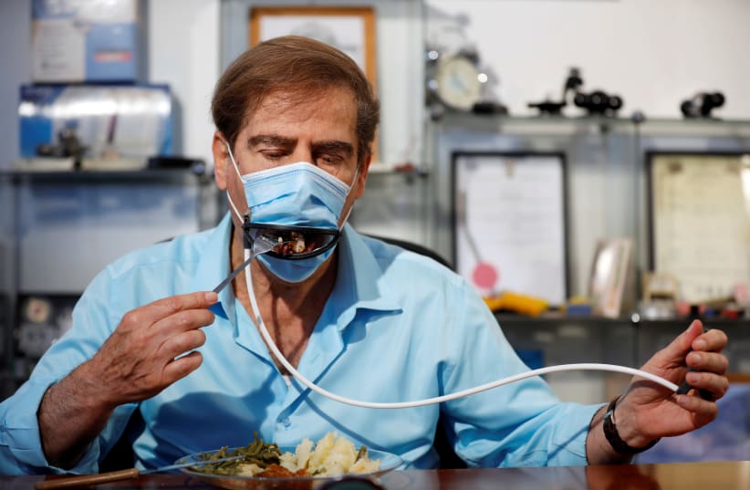 Meir Gitelis, co-developer of an Israeli company, eats while wearing a mask fitted with a mechanical mouth that opens to enable diners to eat without taking it off, as the coronavirus disease (COVID-19) restrictions ease, at Avtipus Patents and Inventions lab in Or Yehuda, Israel May 18, 2020 (photo credit: AMIR COHEN/REUTERS)