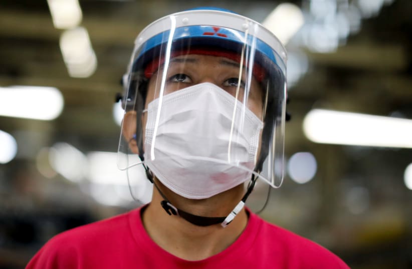 An employee wearing a protective face mask and face guard works on the automobile assembly line during the outbreak of the coronavirus disease (COVID-19) at the factory of Mitsubishi Fuso Truck and Bus Corp. in Kawasaki (photo credit: REUTERS)