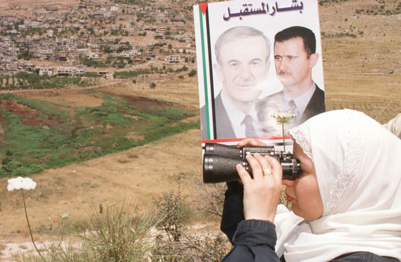 A SYRIAN woman from the Golan Heights village of Ain al-Tinaeh holds a poster of deceased Syrian president Hafez Assad and son Bashar as she searches for relatives in the village of Majdal Shams, across the border in Israel, in July 2000 (photo credit: KH.H/REUTERS)