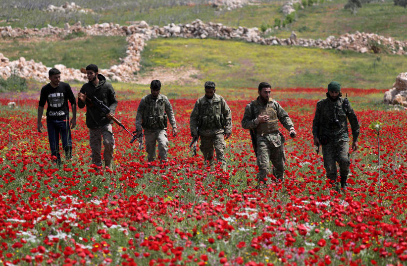 TURKEY-BACKED Syrian rebel fighters walk through a field of flowers in Idlib’s southern countryside, in Syria in April (photo credit: KHALIL ASHAWI / REUTERS)