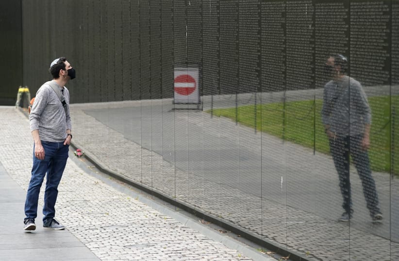 A coronavirus warning sign is reflected as self-proclaimed history buff Amitai Zuckerman from Maryland pays a visit to the Vietnam Veterans Memorial on the day when coronavirus deaths in the U.S. surpassed the 58,220 Americans killed in the Vietnam War, in Washington, U.S., April 29, 2020 (photo credit: REUTERS/KEVIN LAMARQUE)
