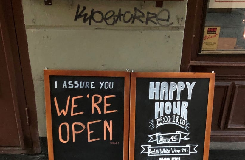  A sign assures people that a pub is open during the coronavirus outbreak in Stockholm, Sweden, March 26, 2020. (photo credit: REUTERS/COLM FULTON/FILE PHOTO)
