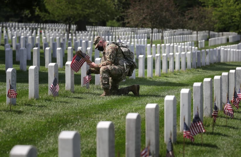 A U.S. Army Old Guard member carries small American flags to place in front of the headstones of U.S. service members buried at Arlington National Cemetery in Arlington, Virginia, U.S., May 21, 2020.  (photo credit: TOM BRENNER/REUTERS)
