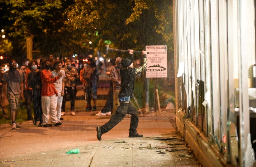 A protester vandalizes an O'Reilly's near the Minneapolis Police third precinct, where demonstrators gathered after a white police officer was caught on a bystander's video pressing his knee into the neck of African-American man George Floyd, who later died at a hospital, in Minneapolis (photo credit: REUTERS/NICHOLAS PFOSI)