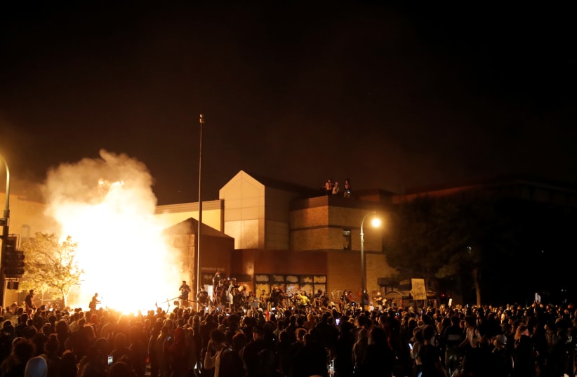 Protesters gather around after setting fire to the entrance of a police station as demonstrations continue in Minneapolis (photo credit: CARLOS BARRIA / REUTERS)