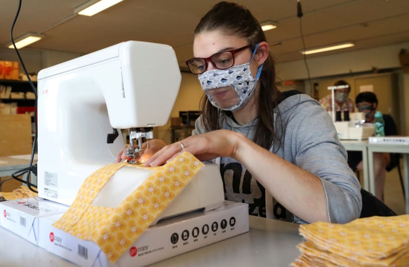 A worker of the bookbinding factory "Brochage-Renaitre", which employs mainly people with disabilities, sews a special protective mask designed with a partially transparent area that allows deaf people to read lips, amid the coronavirus disease (COVID-19) outbreak, in Brussels, Belgium, May 19, 2020 (photo credit: REUTERS)