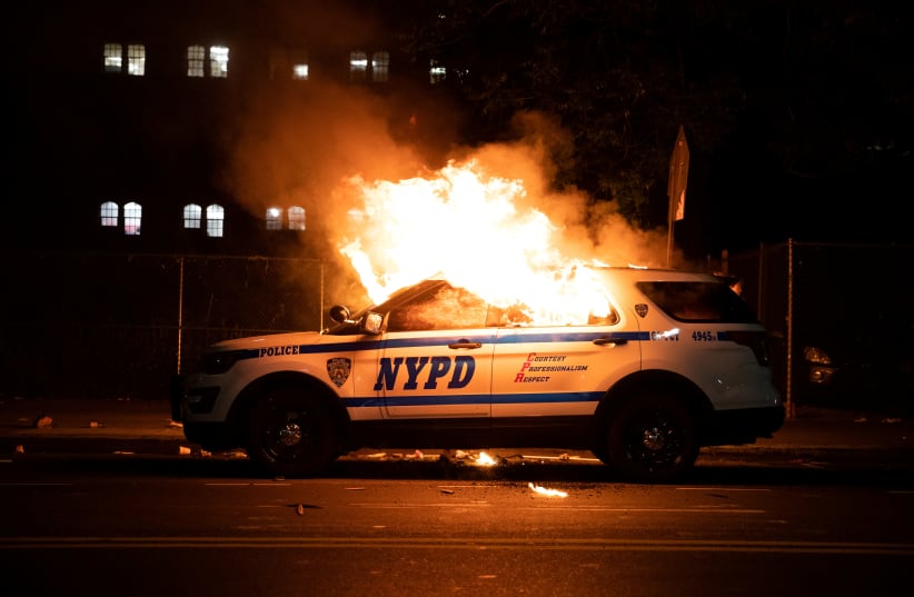 A NYPD police car is set on fire as protesters clash with police during a march against the death in Minneapolis police custody of George Floyd, in the Brooklyn borough of New York City, U.S., May 30, 2020.  (photo credit: JEENAH MOON/REUTERS)