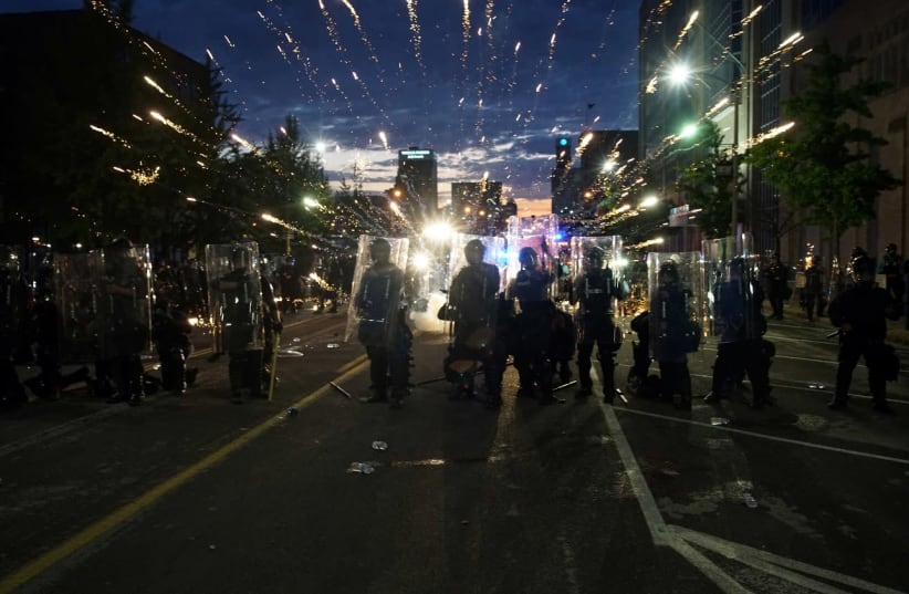Fireworks explode behind police officers during a protest against the death in Minneapolis police custody of African-American man George Floyd, in St Louis, Missouri, U.S., June 1, 2020.  (photo credit: REUTERS/LAWRENCE BRYANT)