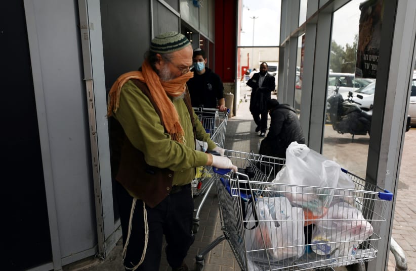 A man wearing gloves and a scarf covering his nose and mouth leaves after shopping at a supermarket ahead of the Jewish holiday of Passover, amid the coronavirus disease (COVID-19) outbreak in Jerusalem April 7, 2020. (photo credit: AMMAR AWAD/REUTERS)