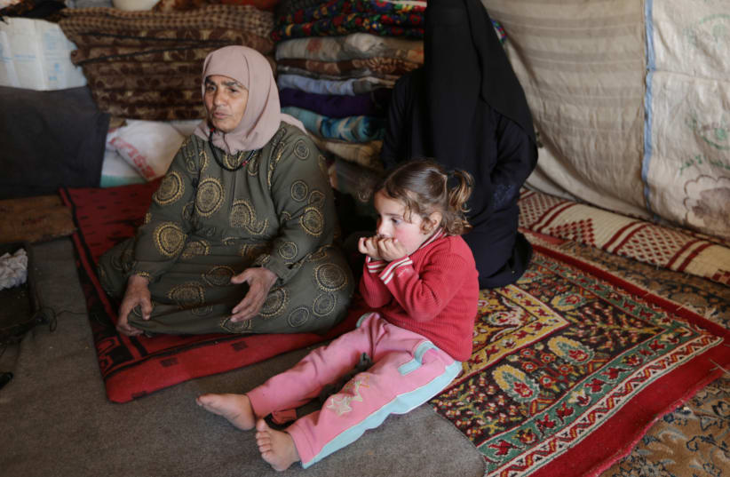 An internally displaced woman, sits with her relatives inside a tent near the town of Afrin, Syria, February 17, 2020 (photo credit: REUTERS/KHALIL ASHAWI/FILE PHOTO)