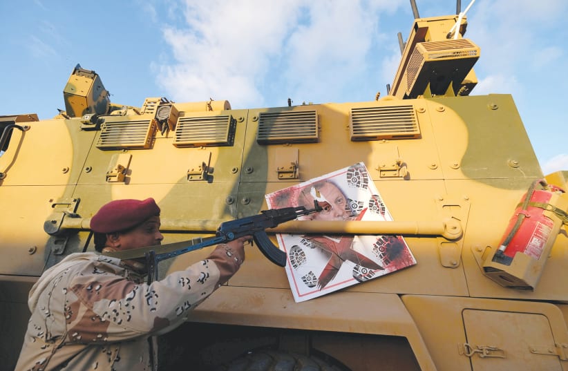 A MEMBER of Libyan National Army (LNA) commanded by Khalifa Haftar, points his gun at an image of Turkish President Tayyip Erdogan on a Turkish military armored vehicle, which the LNA said they confiscated during Tripoli clashes. (photo credit: REUTERS)