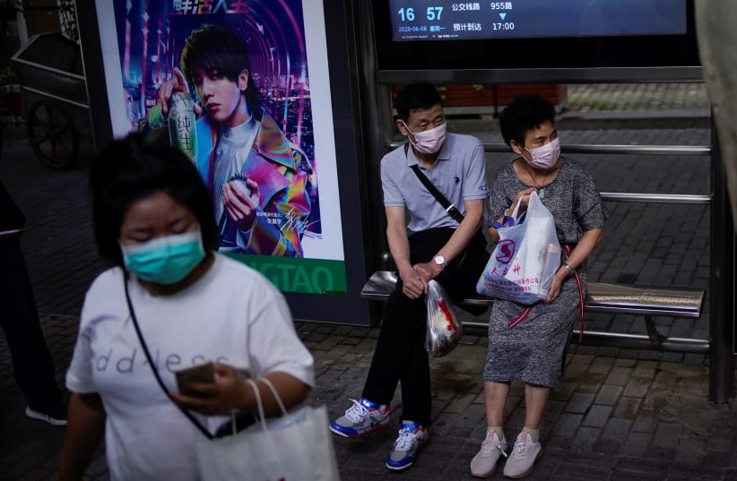 People wearing face masks wait for a bus on a street in Shanghai, following the coronavirus disease (COVID-19) outbreak, China June 8, 2020 (photo credit: REUTERS/ALY SONG)