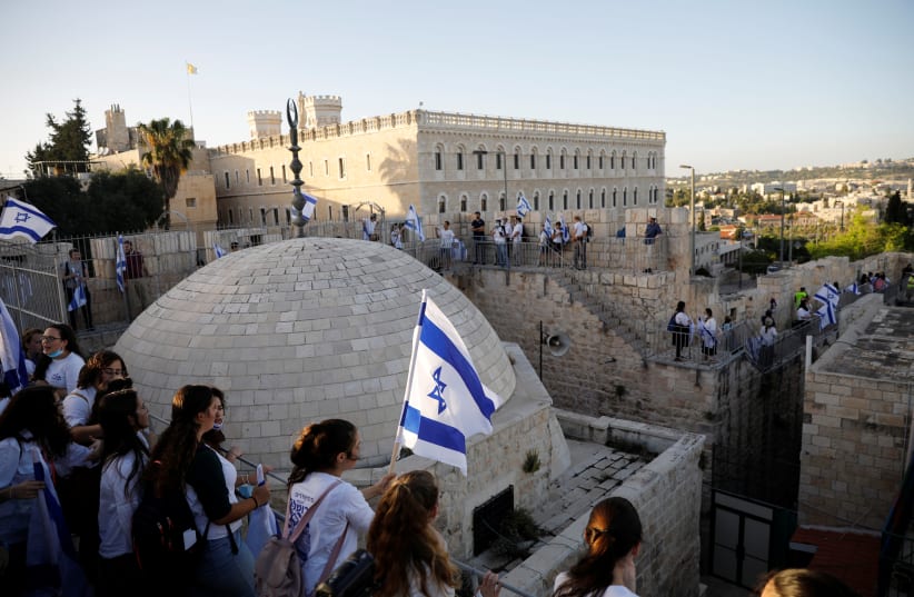 Israelis hold flags and walk on the walls surrounding Jerusalem’s Old City while celebrating Jerusalem Day on May 21 (photo credit: RONEN ZVULUN / REUTERS)