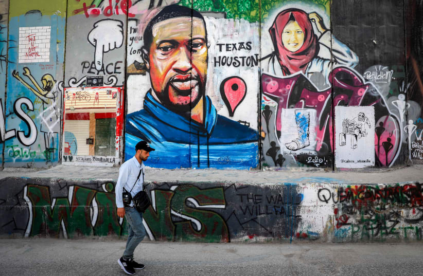 Palestinians walk past graffiti of George Floyd painted on a section of the separation wall in the West Bank city of Bethlehem, on June 8, 2020. (photo credit: WISAM HASHLAMOUN/FLASH90)