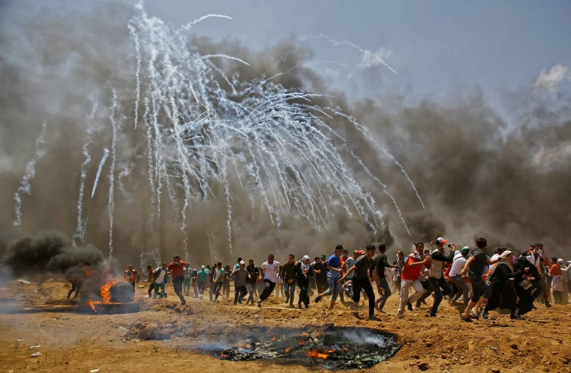 Palestinians run for cover from tear gas during clashes with Israeli security forces near the border between Israel and the Gaza Strip, east of Jabalia on May 14, 2018 (photo credit: MOHAMMED ABED/AFP/GETTY IMAGES)