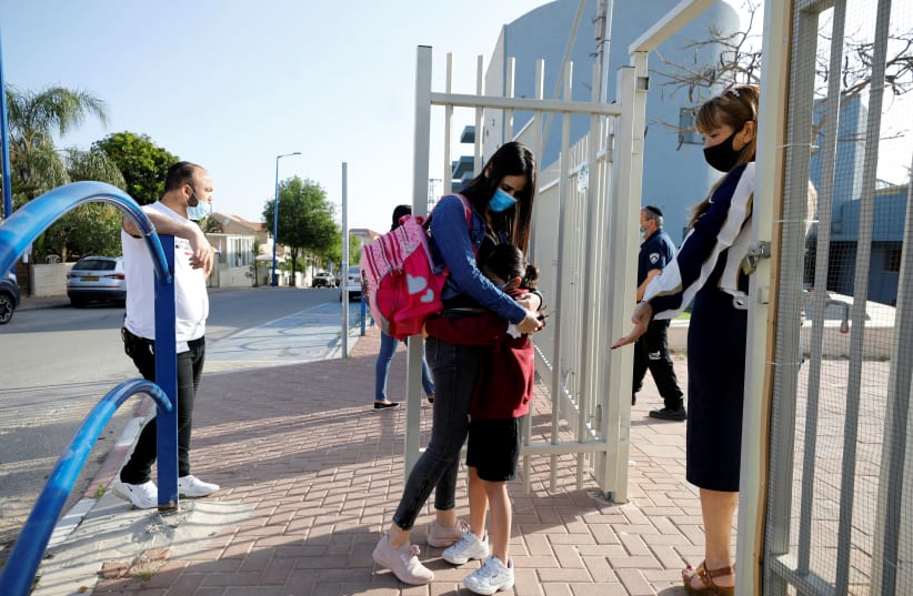 A girl hugs her mother before entering her elementary school in Sderot as it reopens following the ease of restrictions preventing the spread of the coronavirus disease. (photo credit: REUTERS/AMIR COHEN)