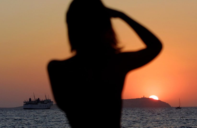 A woman photographs the setting sun on the Spanish island of Ibiza August 29, 2001. Ibiza, one of the most popular tourist attractions in Spain, was hosting the all-night MTV Ibiza 2001 party at Privilege disco which claims to be the largest in the world. (photo credit: REUTERS)